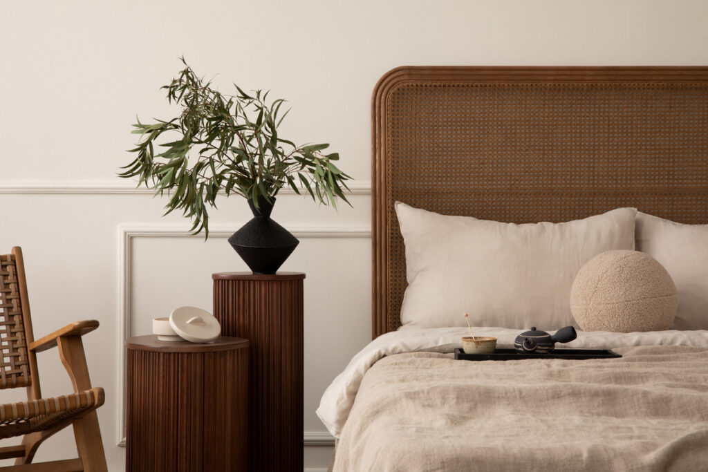 Bedroom with a neatly made bed, green plant, table lamp, and subtle sunlight